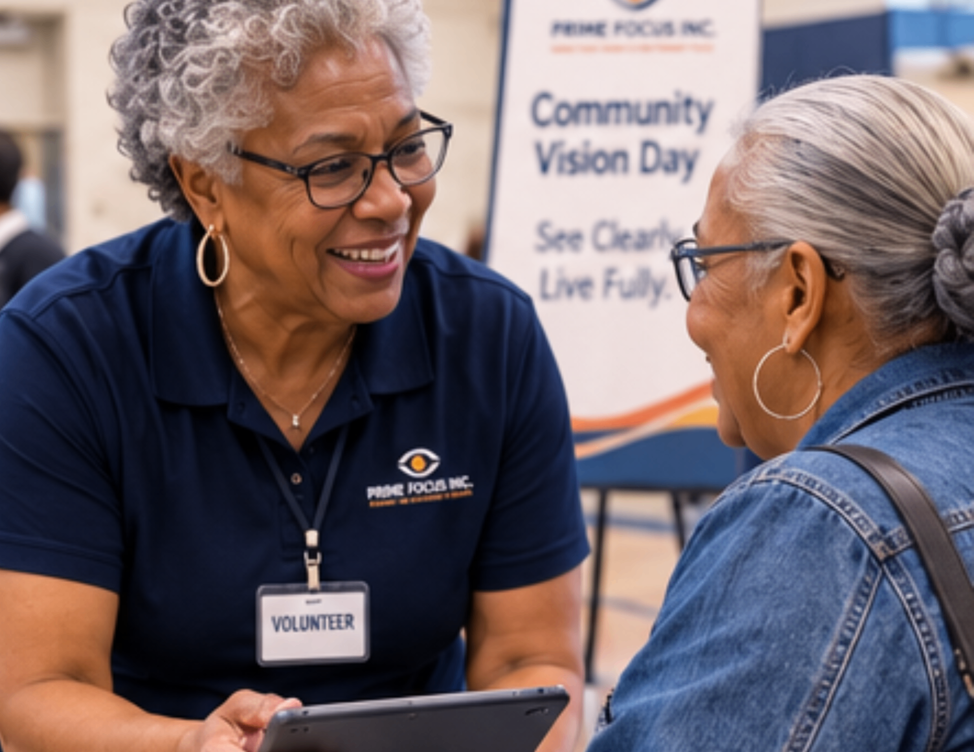 A Prime Focus volunteer smiles while speaking one-on-one with a family member at the event registration table.